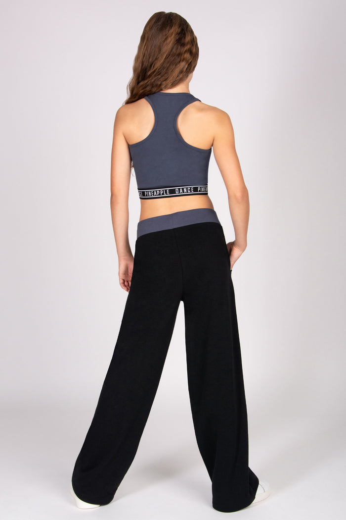 Girl wearing a dark grey sports bra and black wide trousers on a white background