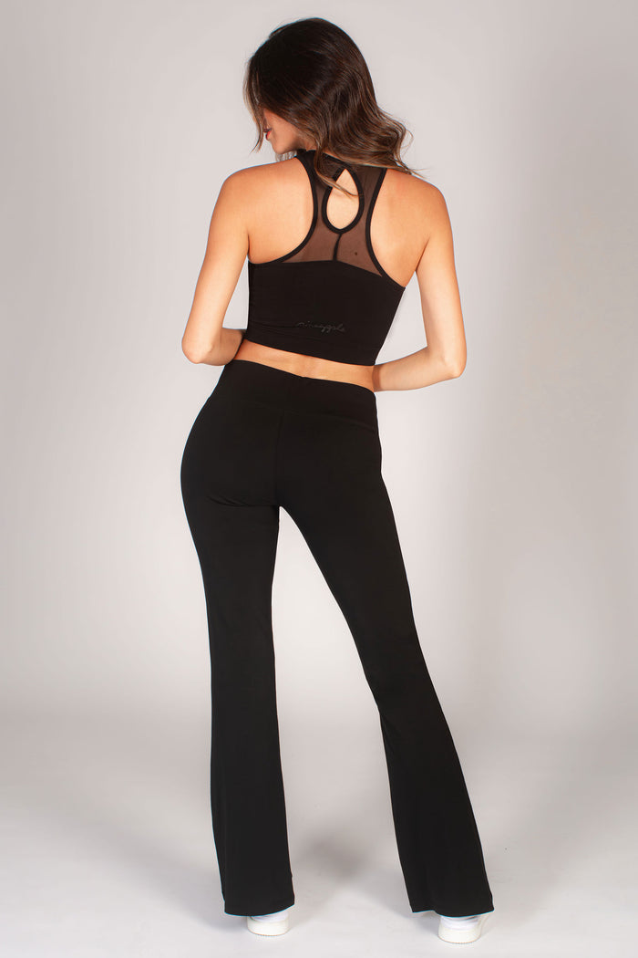 Black flared stretchy leggings for women paired with a mesh panel crop top by Pineapple Dance Studios.