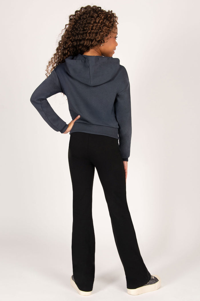 Girl wearing a charcoal hoodie and black flared trousers on a white background