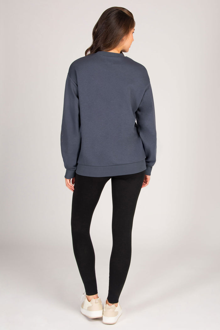 Person wearing a blue sweatshirt and black leggings on a plain background