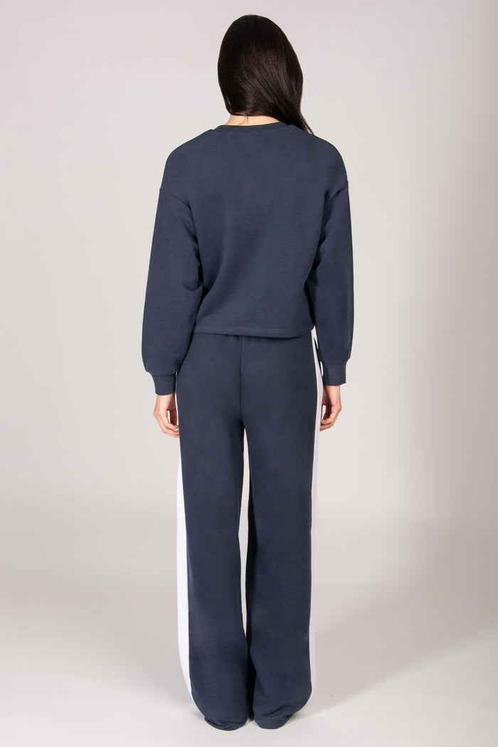 Woman wearing dark grey sweatshirt and wide leg trousers on a light grey background.