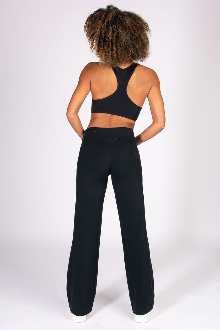 Woman wearing a black super soft wide leg yoga pants with matching sports bra on a white background