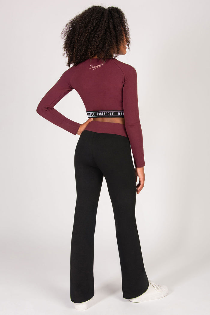 Girl wearing a burgundy long-sleeve crop top and black flared pants on a white background