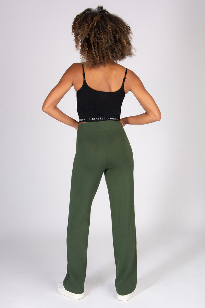 Woman wearing a black tank top and khaki wide leg yoga trousers on a white background
