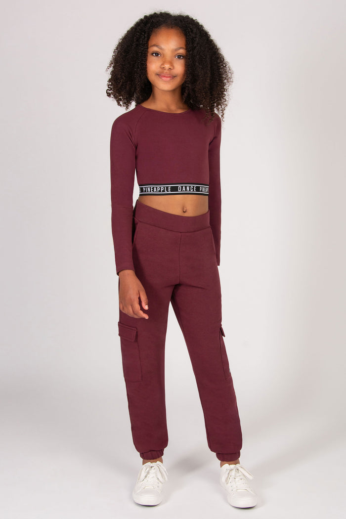 Child wearing a burgundy long-sleeve top and cargo jogger pants on a white background