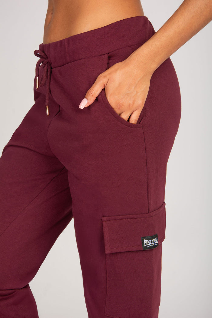 Maroon cargo joggers with pockets and a brand logo on a plain background