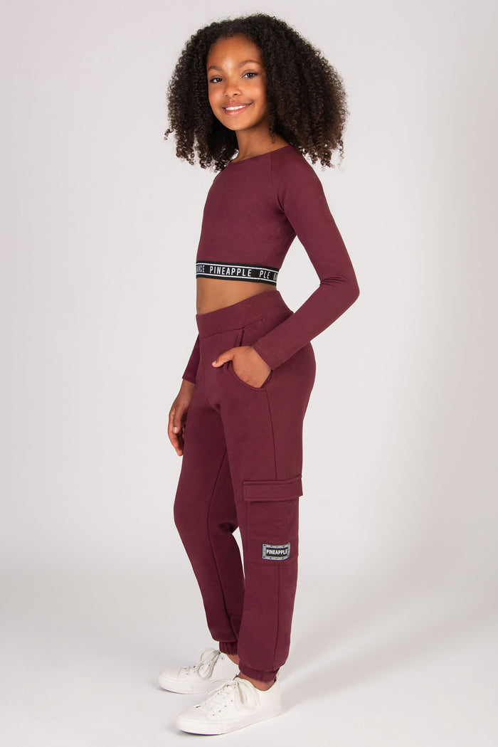 Young girl wearing a burgundy trackpants with pockets on a white background