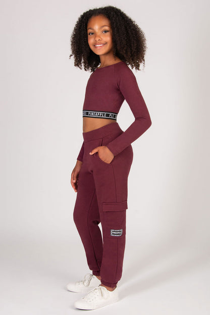 Young girl wearing a burgundy trackpants with pockets on a white background