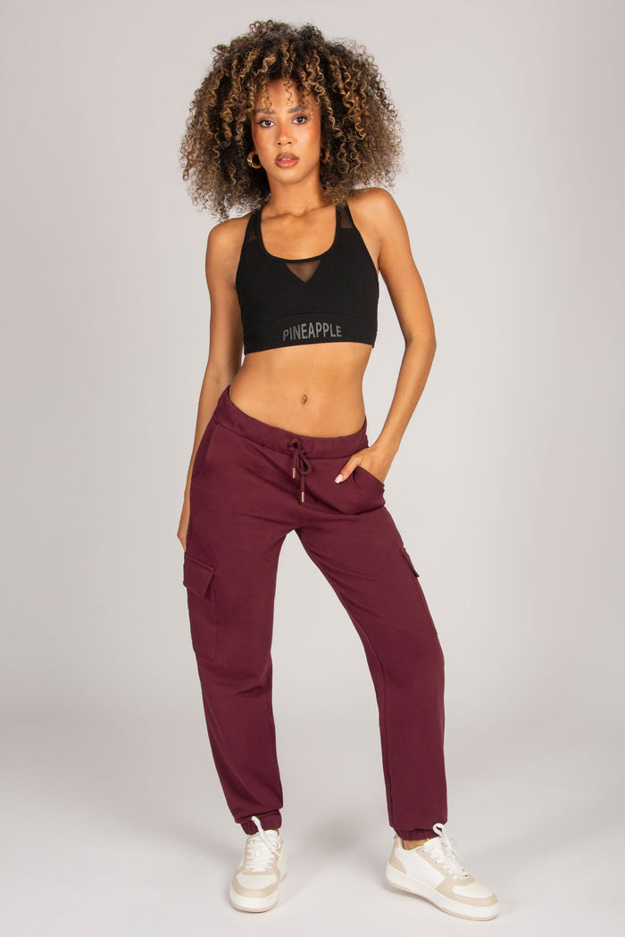 Woman wearing a black sports bra and maroon jogger pants on a plain background