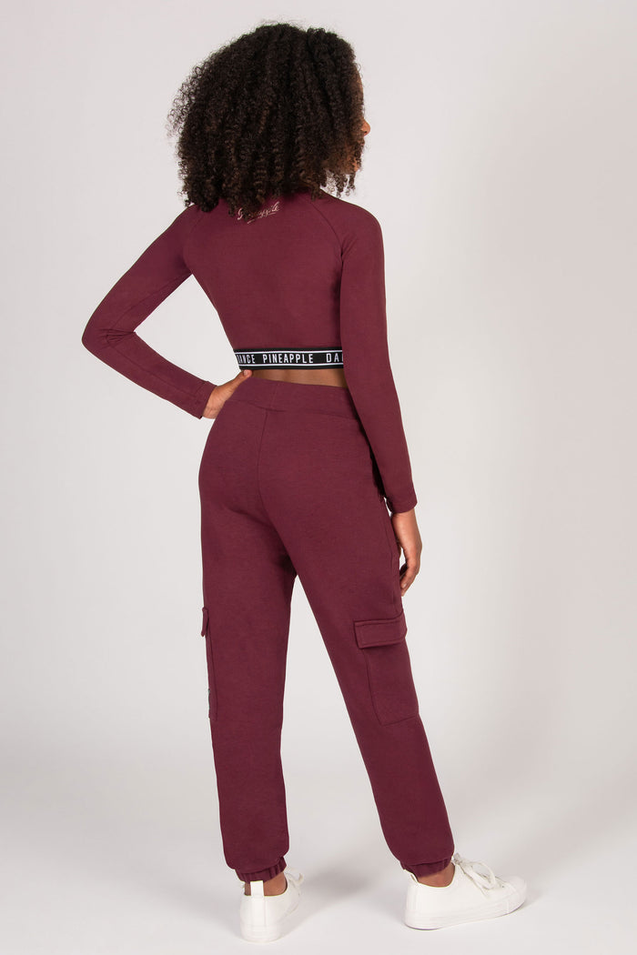 Girl wearing a burgundy pocket cargo joggers and long sleeve top with a white background