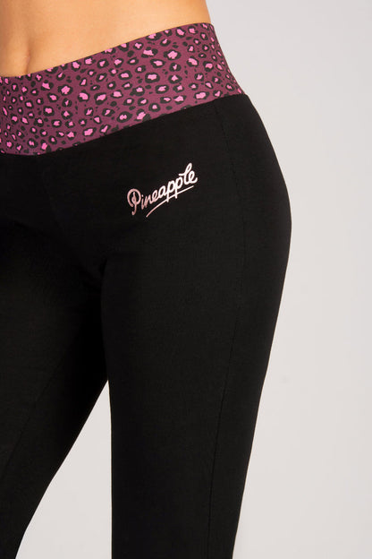 Black flared leggings with a burgundy leopard print waistband and 'Pineapple' branding by hip