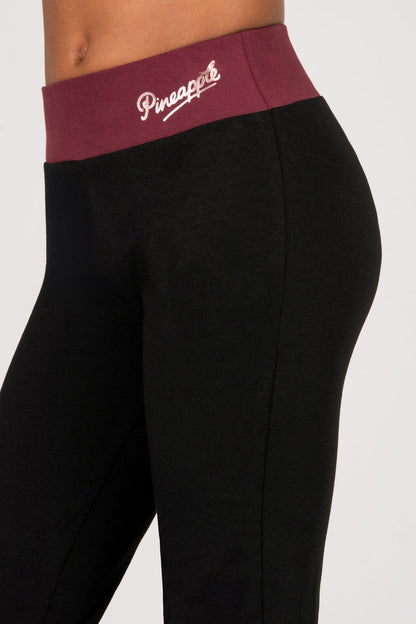 Black flared leggings with a maroon waistband featuring 'Pineapple' branding on a white background.