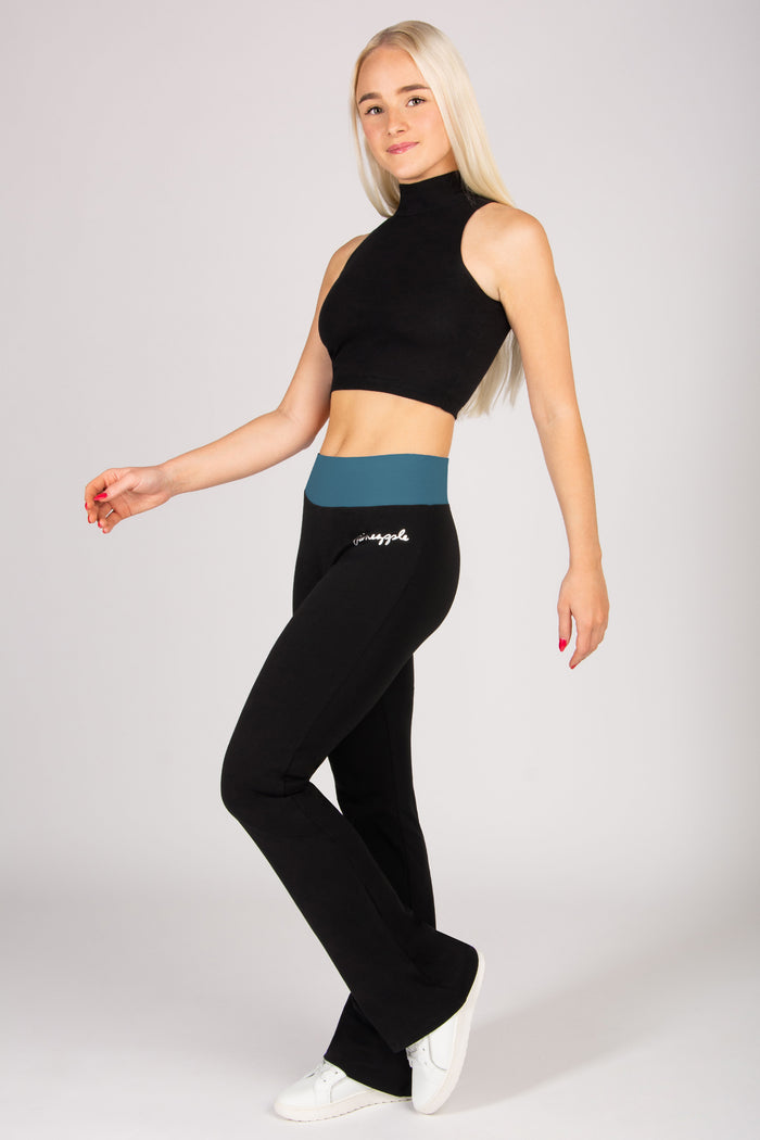 Woman wearing black high-neck top and black flared leggings with a blue waistband on a white background