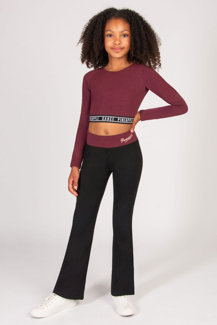 Girl wearing a burgundy long-sleeve top and black flared leggings on a white background