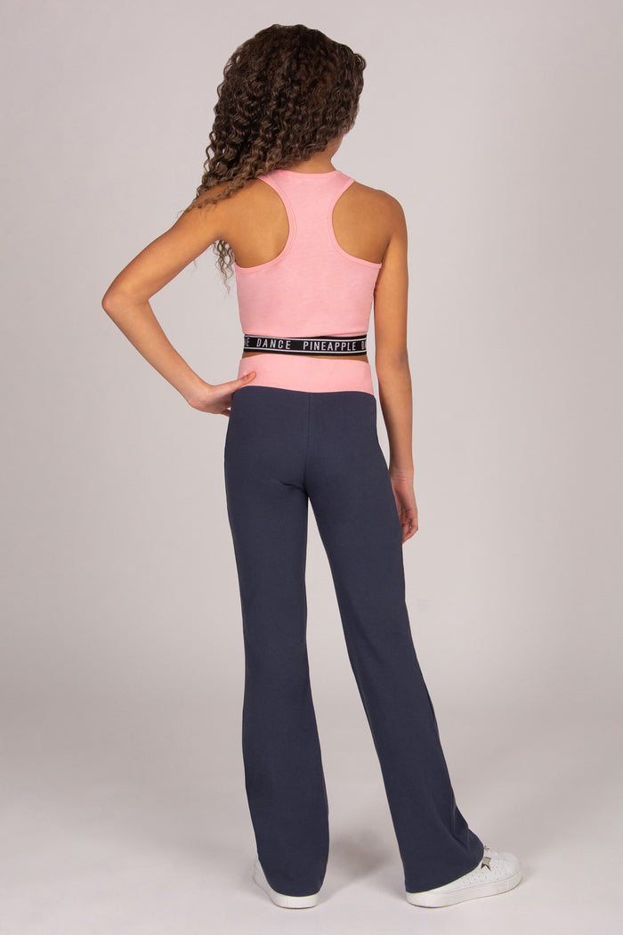 Girl wearing light pink sports crop top with matching dark grey bootcut trousers on plain background.