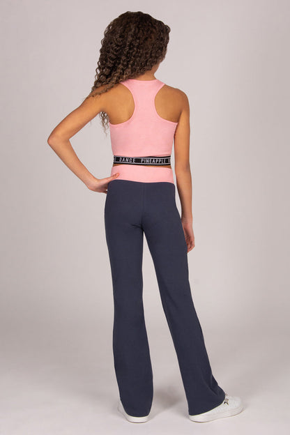 Girl wearing light pink sports crop top with matching dark grey bootcut trousers on plain background.