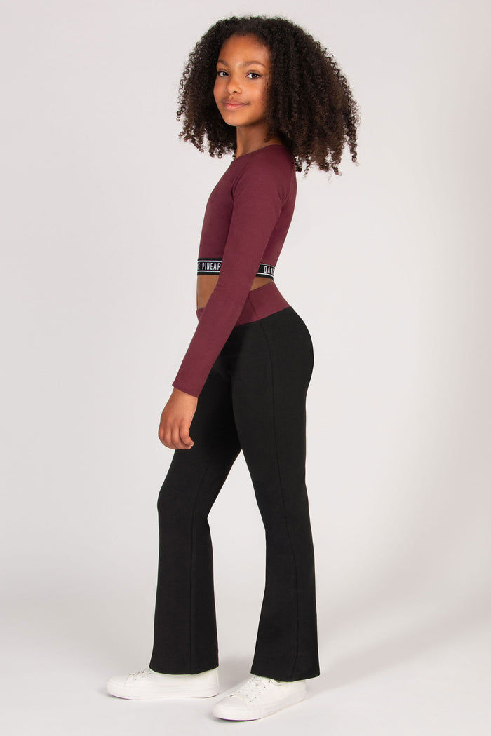 Girl wearing a burgundy long-sleeve top and black flared trousers on a white background