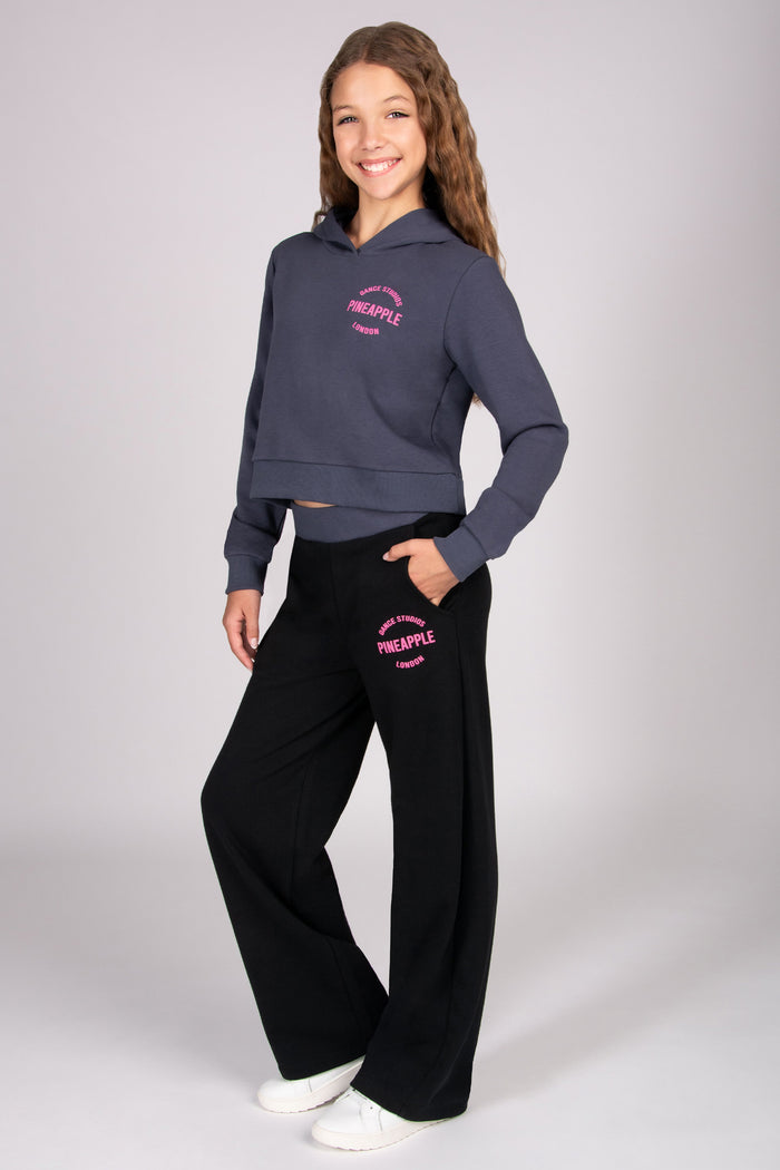 Girl wearing a dark grey hoodie and black wide leg trousers with pocket on white background