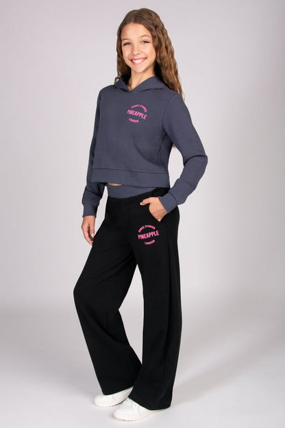 Girl wearing a dark grey hoodie and black wide leg trousers with pocket on white background