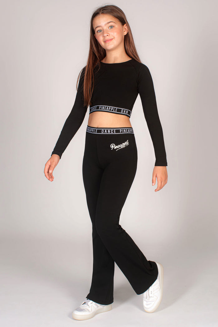 girl wearing Pineapple black flared jersey trousers with matching girls' midi long sleeve crop top