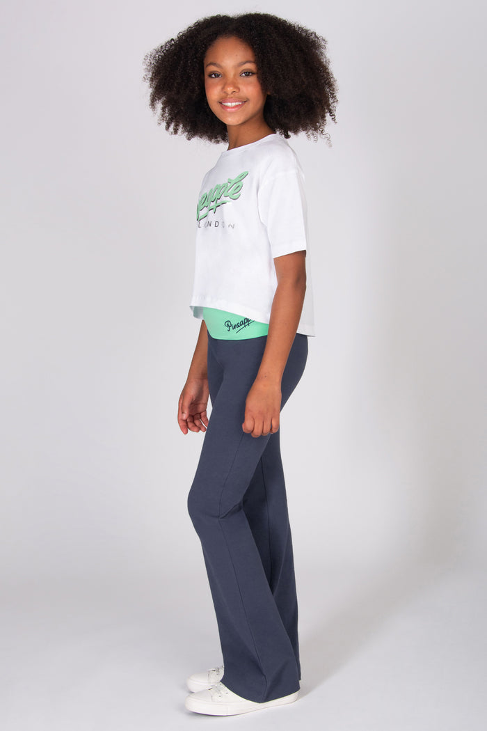 Teenager wearing a white crop t-shirt and dark  grey flared pants on a plain background