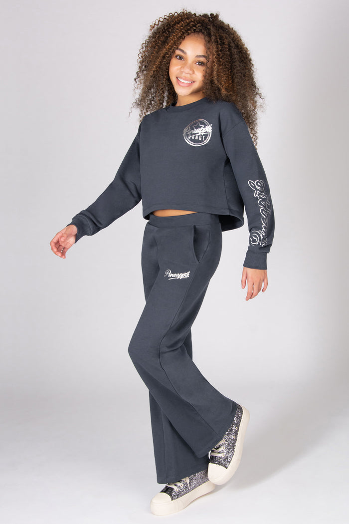 Girl wearing a dark grey sweatshirt and wide leg pants on a white background