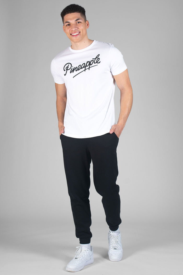 Man wearing white T-Shirt with black logo and black jogging trousers