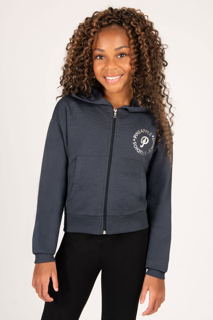 Girl wearing a charcoal blue hoodie with a silver foil logo on a white background