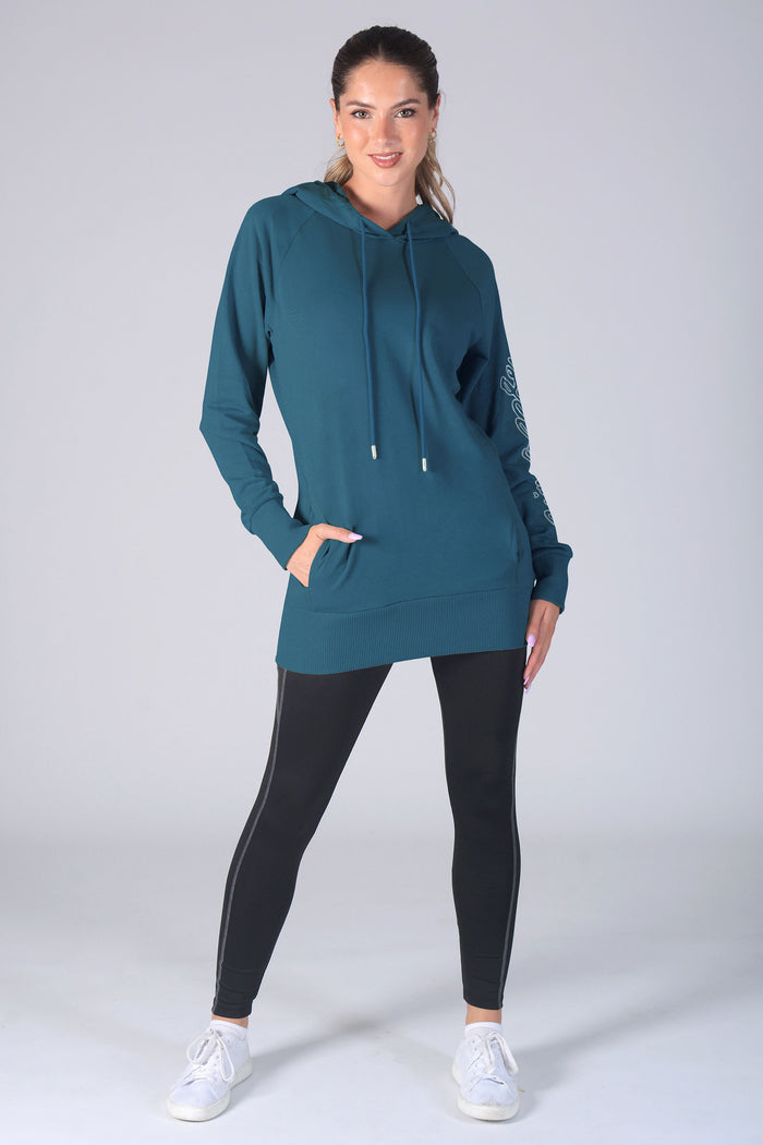 Woman wearing a teal pocket hoodie and black leggings on a white background
