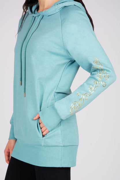 Woman wearing a light blue hoodie featuring side pockets and gold foil print against a plain background