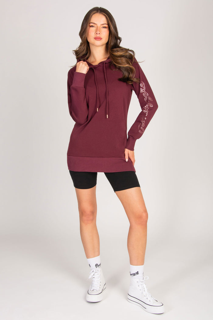 Woman wearing a maroon hoodie and black shorts with Pineapple club socks and trainers on a white background