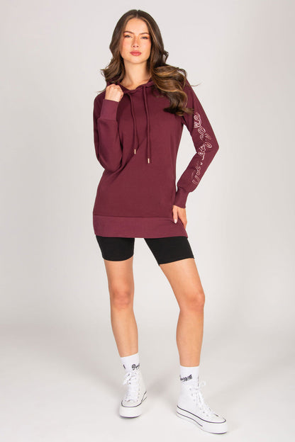 Woman wearing a maroon hoodie and black shorts with Pineapple club socks and trainers on a white background