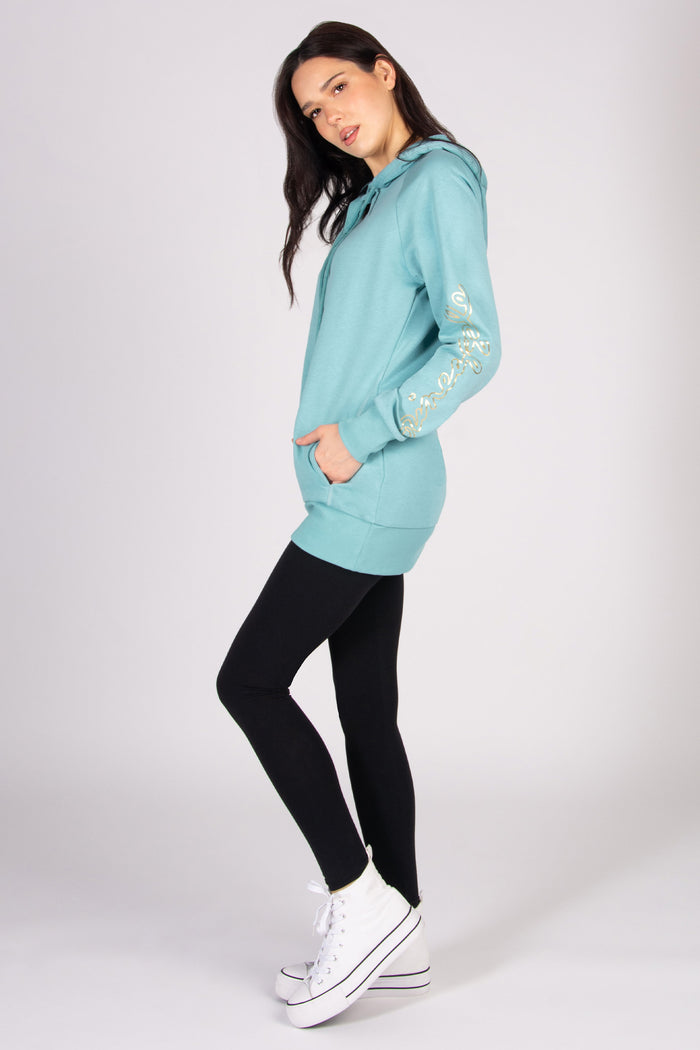 Woman wearing a light blue longline hoodie and black leggings against a plain background