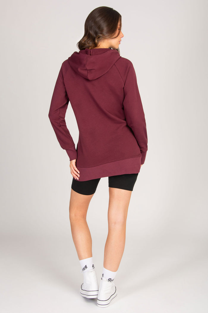Woman wearing a maroon hoodie and black cycling shorts on a plain background