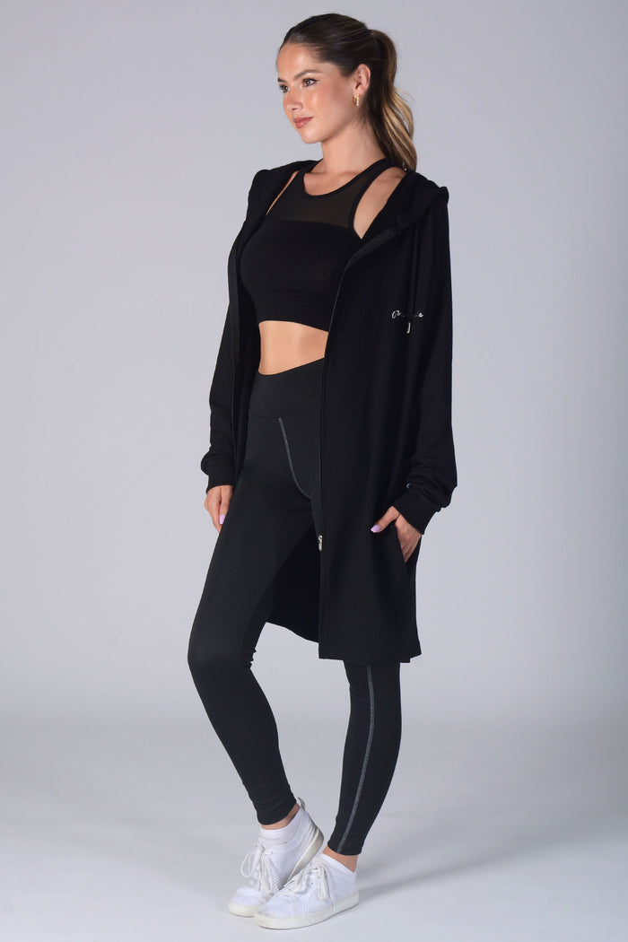 Woman wearing black Longline Hooded Zip Jacket, black Monroe crop top, and black leggings with pockets