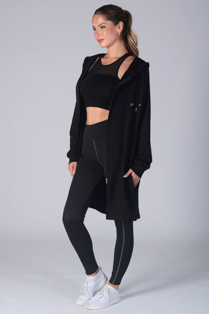 Woman wearing black Longline Hooded Zip Jacket, black Monroe crop top, and black leggings with pockets