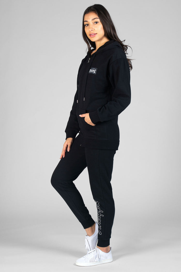 Woman wearing black Loopback Joggers, white vest and black Badge Zip Hoodie