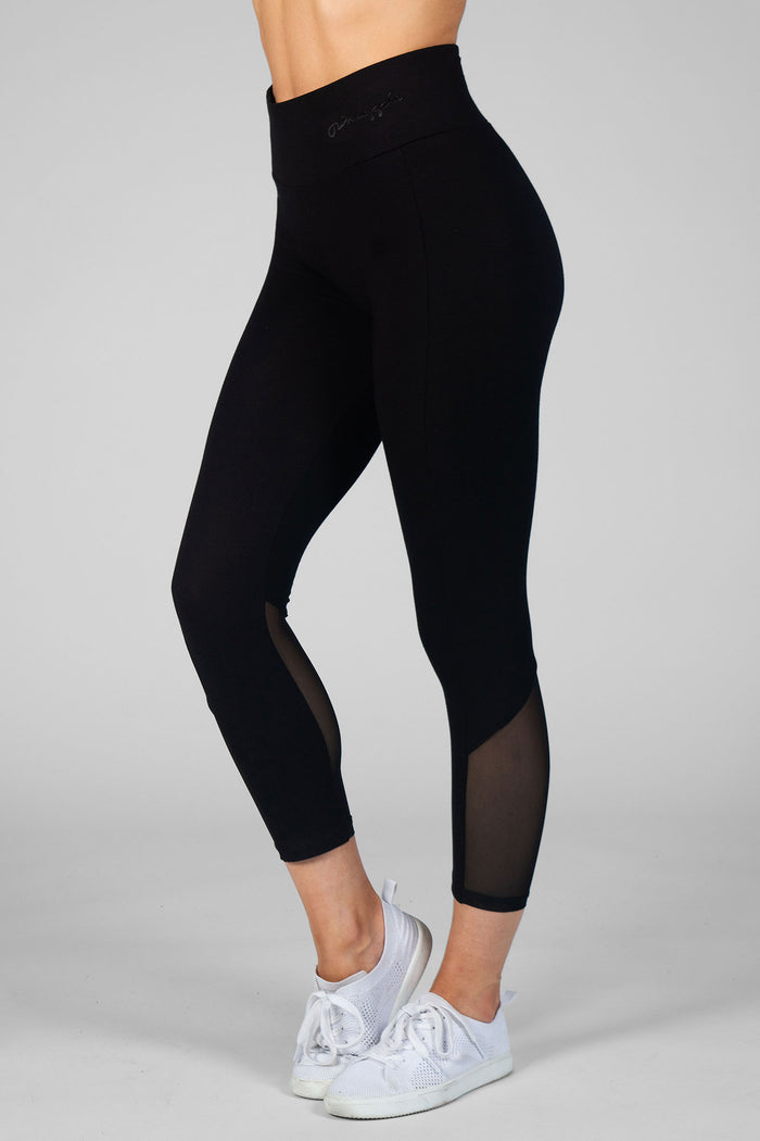 Woman wearing black crop leggings with mesh paneling against a grey backdrop