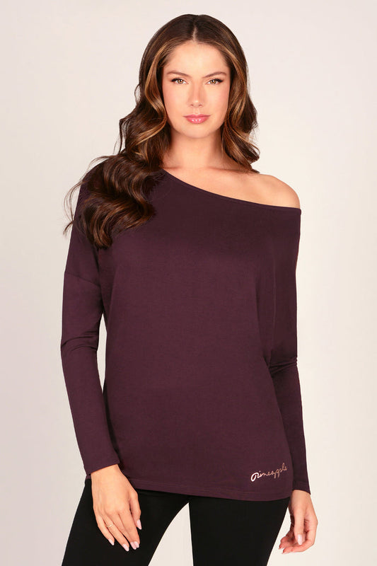 Woman wearing a maroon brown off-shoulder tunic top with long sleeves on a plain background.
