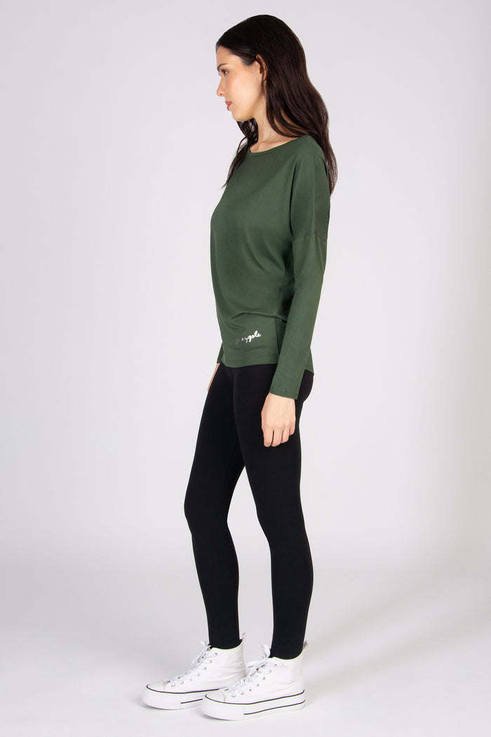 Woman wearing a khaki long sleeve top and black leggings on a white background
