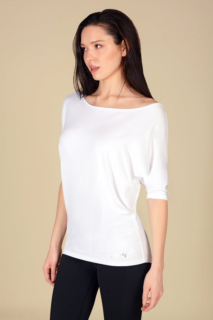 Woman wearing a white top and black leggings against a beige background