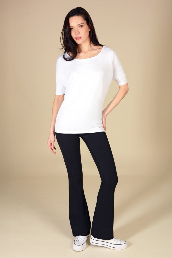 Woman wearing a white jersey short sleeve top and black flares on a beige background