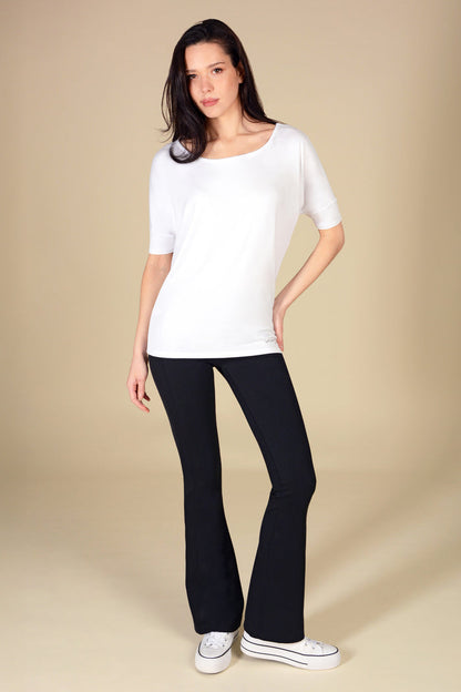 Woman wearing a white jersey short sleeve top and black flares on a beige background