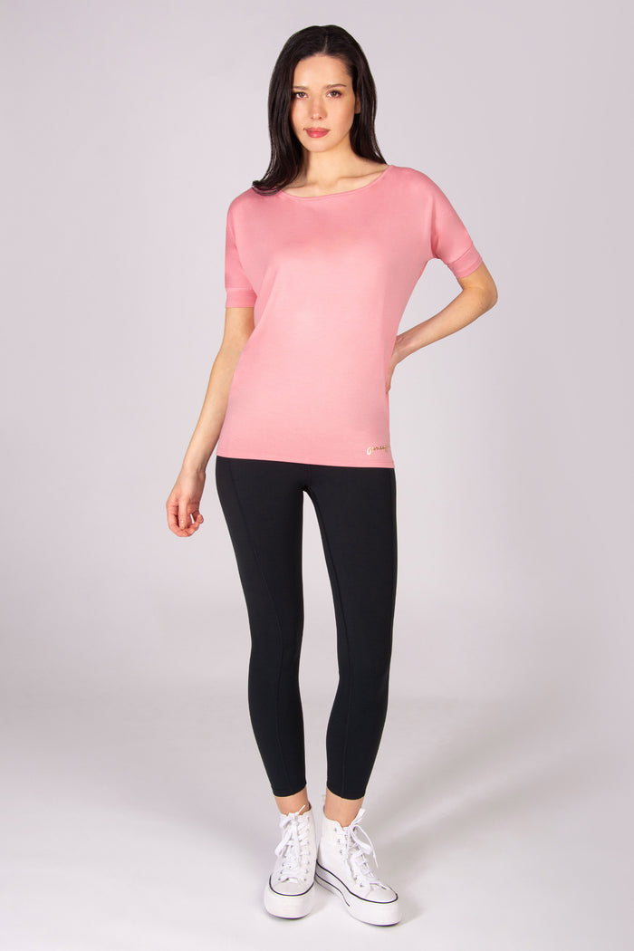 Woman wearing a coral pink short sleeve top and black leggings on a white background