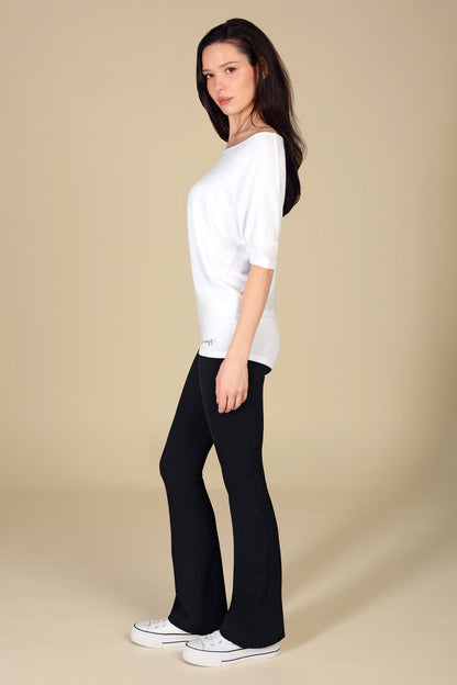 Woman wearing a white jersey top and black flares on a beige background