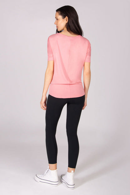 Woman wearing a pink short sleeve top and black leggings on a white background