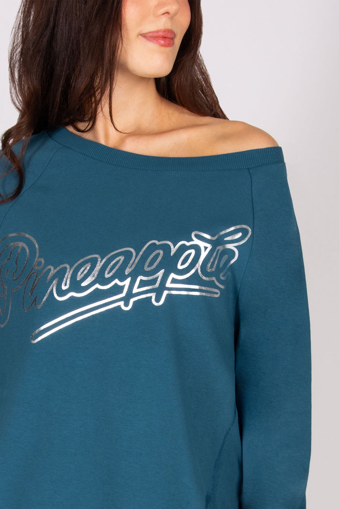Detail of the 'Pineapple" logo print on a teal sweat top.