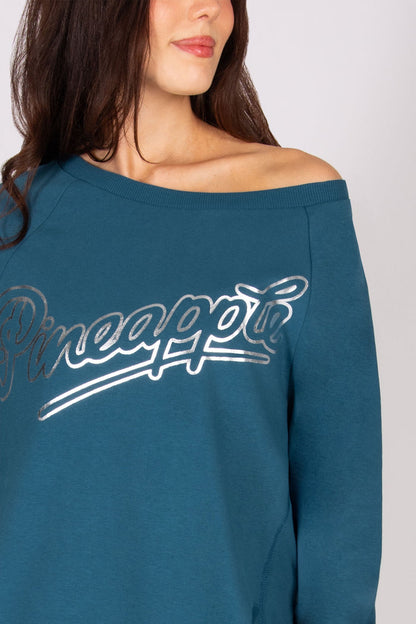 Detail of the 'Pineapple" logo print on a teal sweat top.