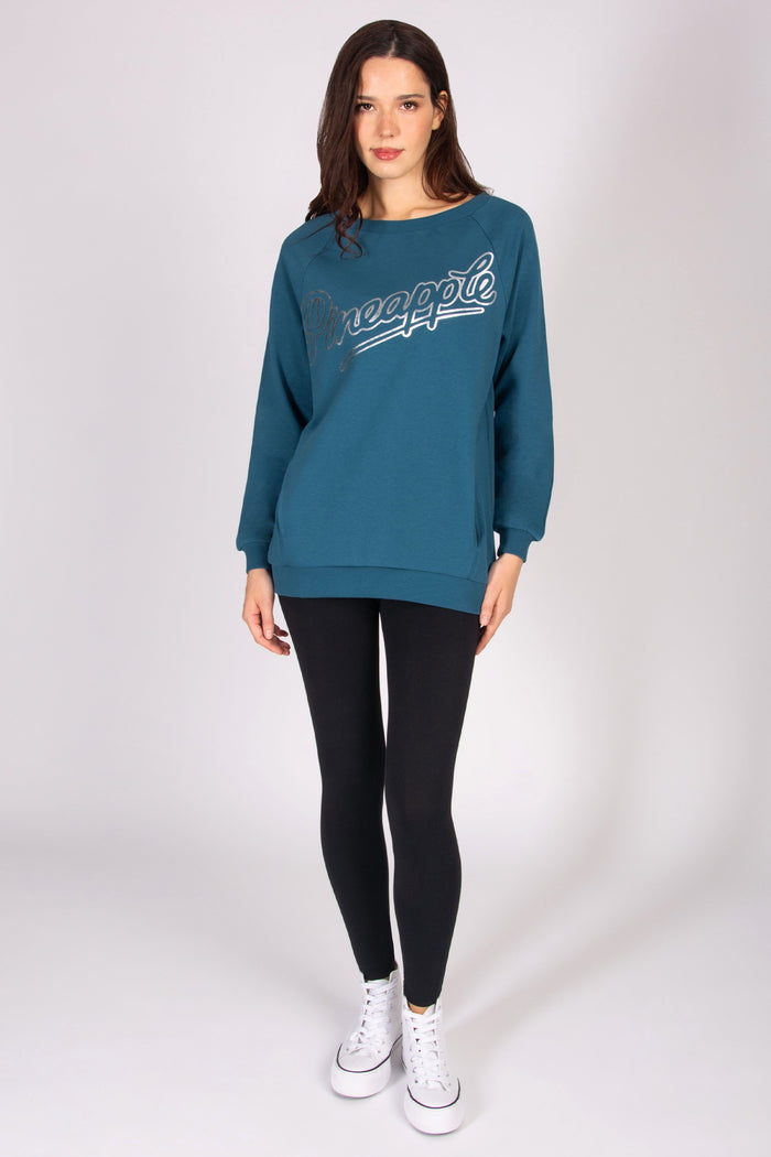 Woman wearing a teal oversized jumper with black leggings and white trainers
