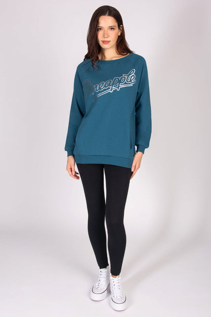 Woman wearing a teal oversized jumper with black leggings and white trainers